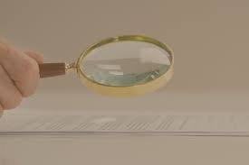 محامي جنائي في الرياض يفحص مستندًا مشتبهًا بتزويره بجانب عدسة مكبرة وملف قضية قبل جلسة بالمحكمة الجزائية